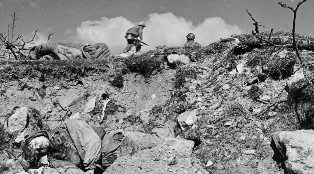 Soldiers of the 10th Mountain Division pass a dead German soldier as they take the crest. US Army.