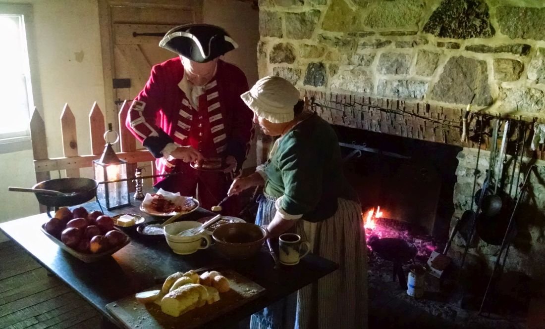 Reenactors enjoy a breakfast of ham and French toast cooked over a fireplace.