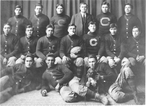 The 1911 Carlisle Indians football team poses with a game ball from the victory against Harvard. Pictured are fullback Jim Thorpe, seated third from right, and head coach Glenn "Pop" Warner, standing third from right.