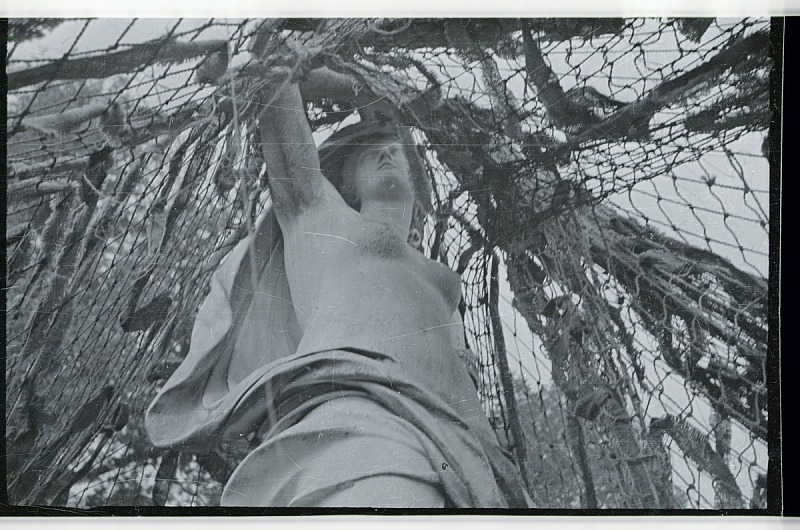 Photographic negative shows a sculpture of a woman covered in camouflage netting, possibly at Versailles.