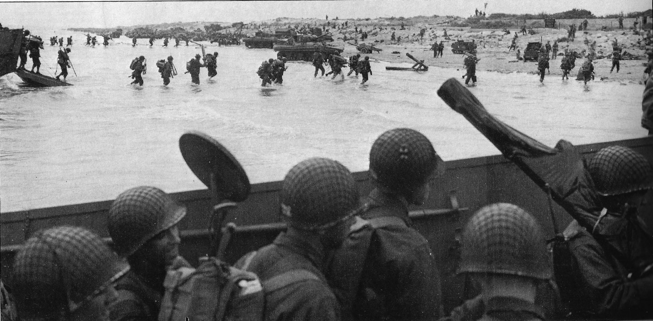 U.S. troops was ashore at Utah Beach on June 5, 1944; in the background, canvas collars collapsed, are Duplex Drive Tanks that made it to the beach. U.S. Coast Guard.