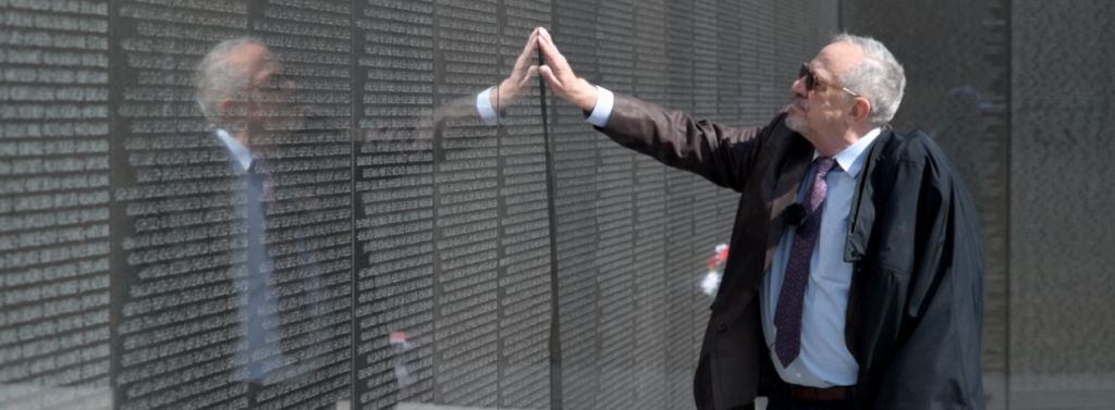 Jan Scruggs touches panel 14W with the names of his 12 friends who died on a day that still haunts him. VA photo by Tass Mimikos.